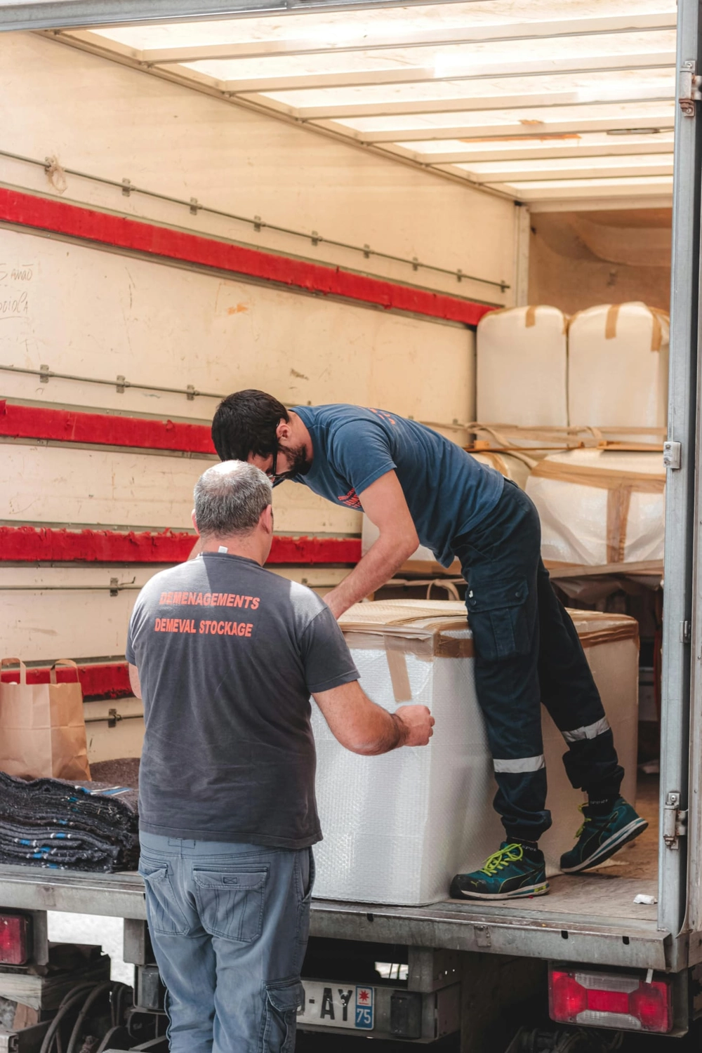 R&O Facilityservice – Zwei Umzugshelfer laden große, verpackte Kartons in einen Lkw, einer im Inneren und einer auf dem Boden.